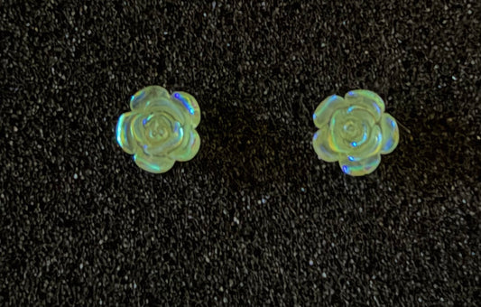 A pair of small rose-shaped stud earrings made of iridescent opal, displayed on a textured black background.