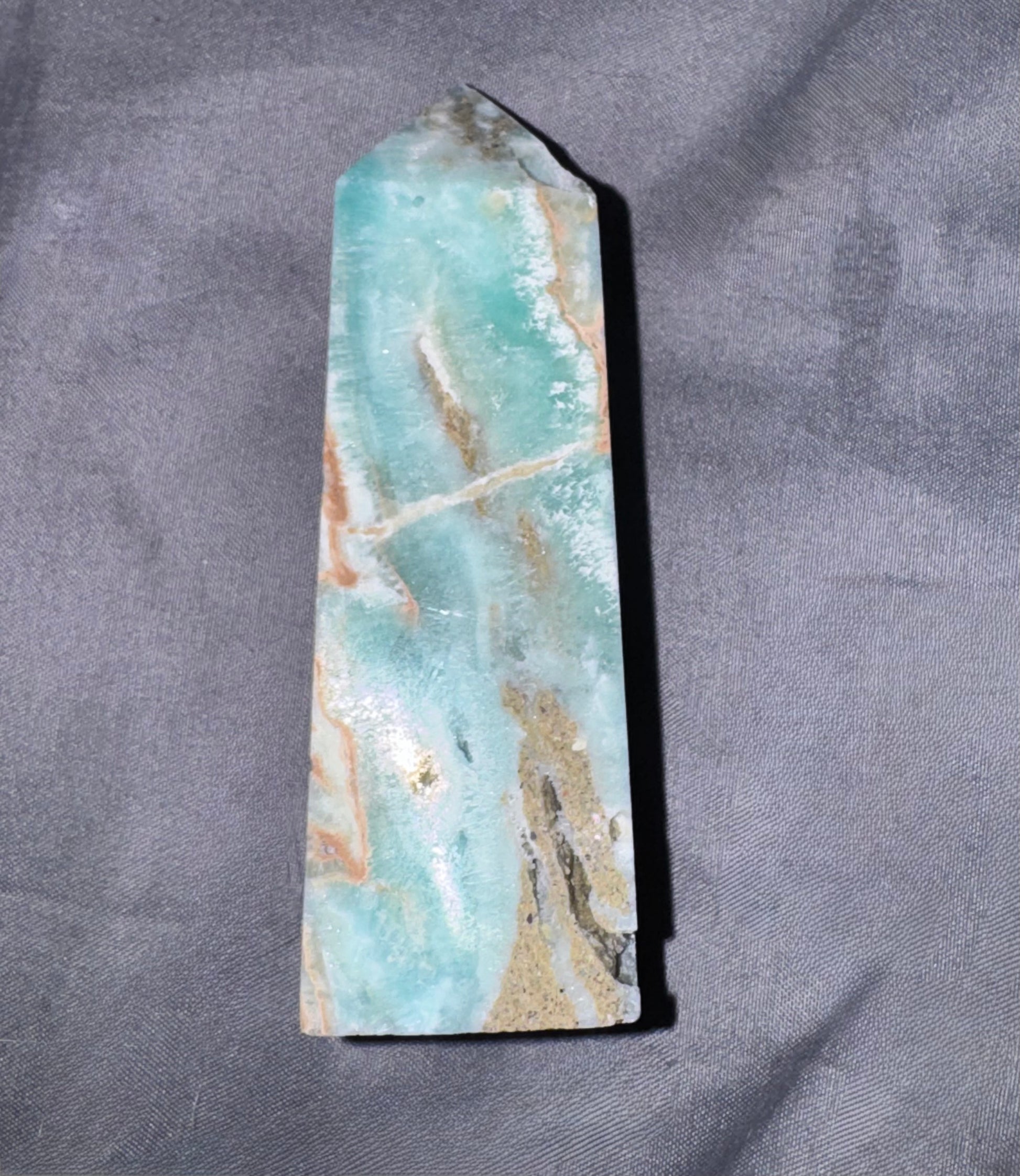 A raw amazonite crystal tower with natural brown and white veining, standing upright on a textured gray fabric background.