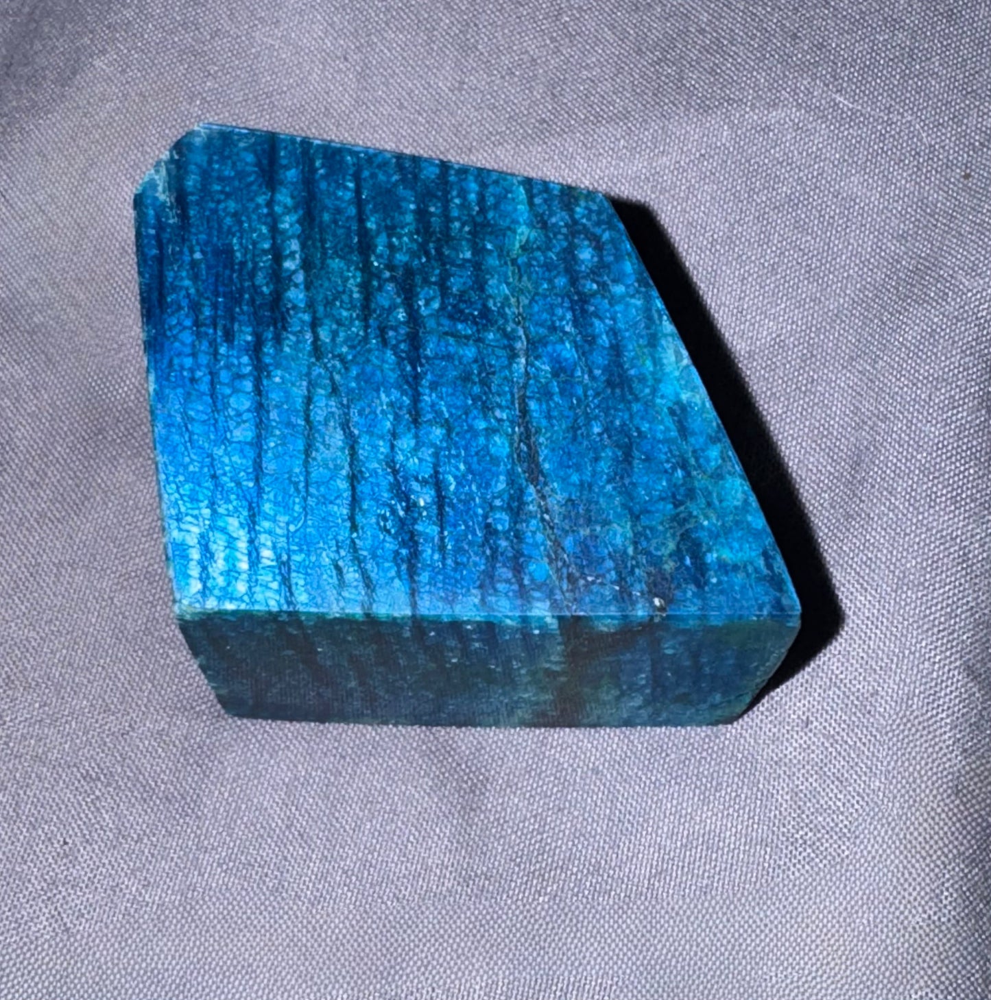 A raw blue labradorite stone chunk with natural striated texture, resting on a gray textured fabric background.
