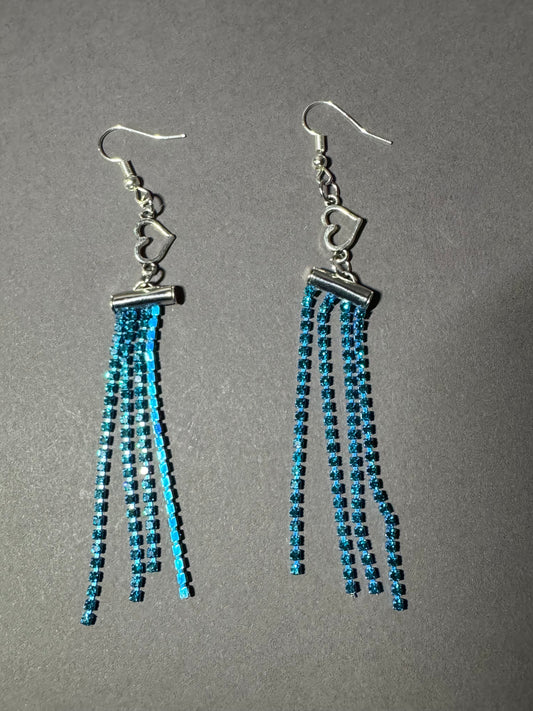 A pair of dangling earrings with silver fishhook wires and multiple strands of small blue beads, photographed on a plain gray background.