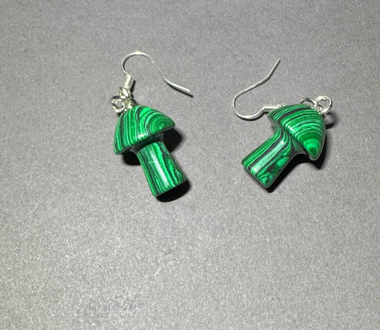 A pair of mushroom-shaped drop earrings made from green malachite with silver fishhook wires, displayed on a textured gray background.