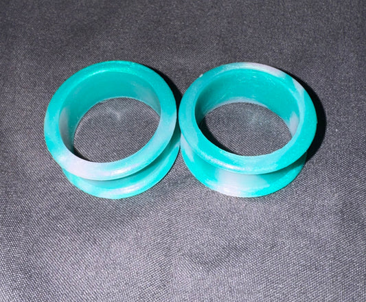Two turquoise and white marbled silicone ear plugs on a dark gray textured fabric background.