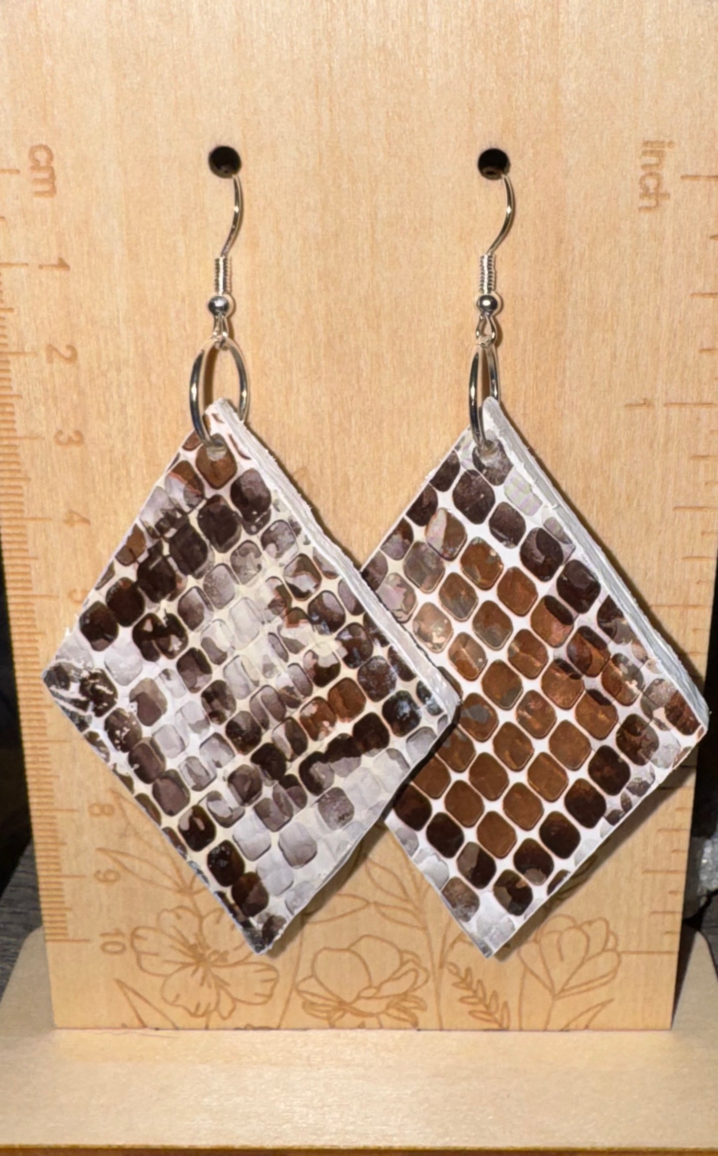 Pair of diamond earrings with brown and white pattern on a wooden surface with ruler.