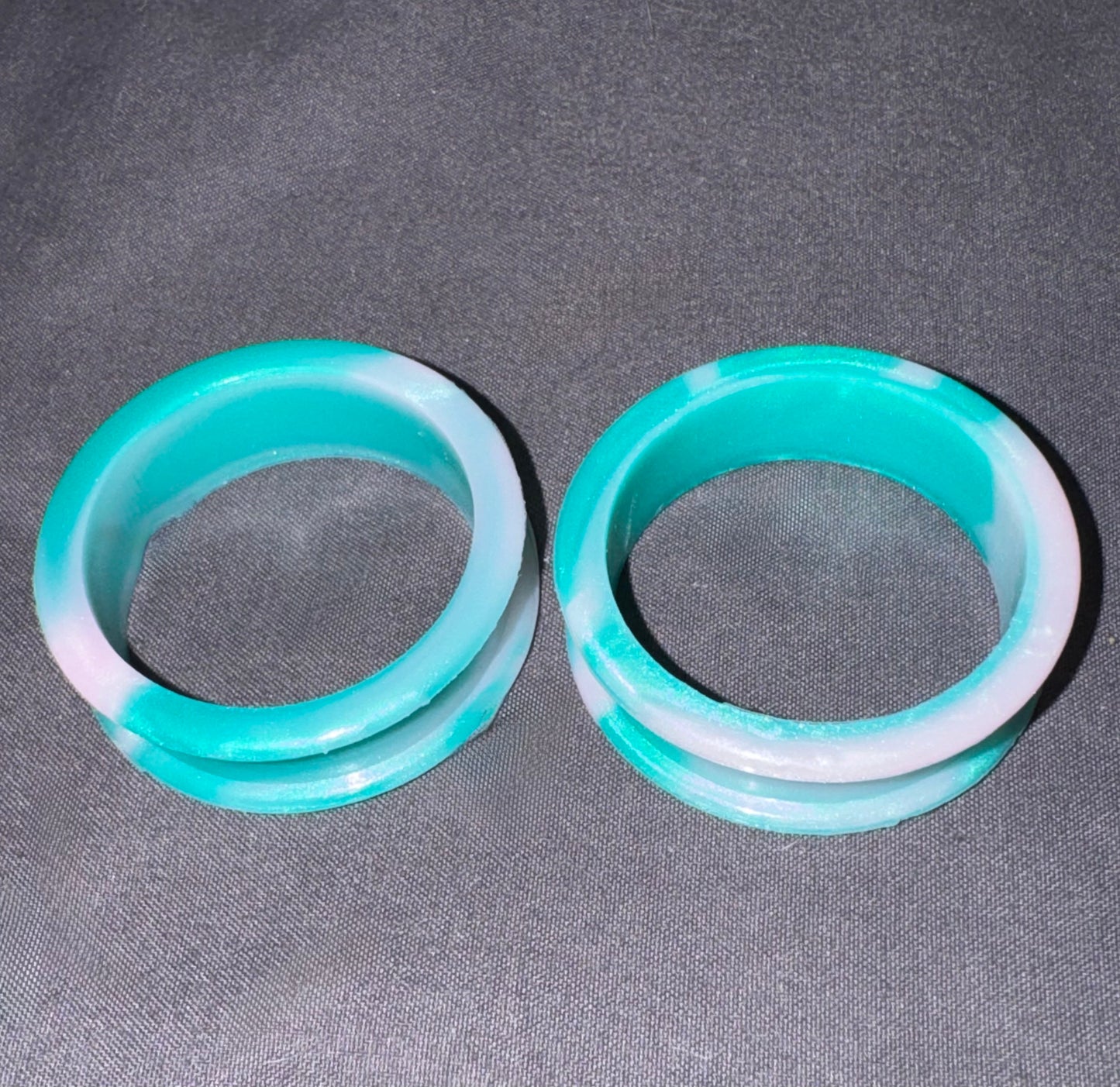 Two round turquoise and white marbled bangles displayed side-by-side on a dark gray textured fabric background.
