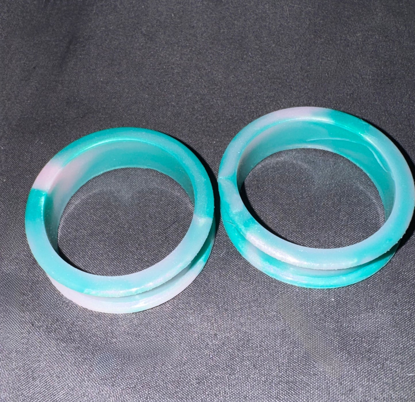 Two semi-translucent turquoise and white bangles displayed side-by-side on a dark gray textured fabric background.