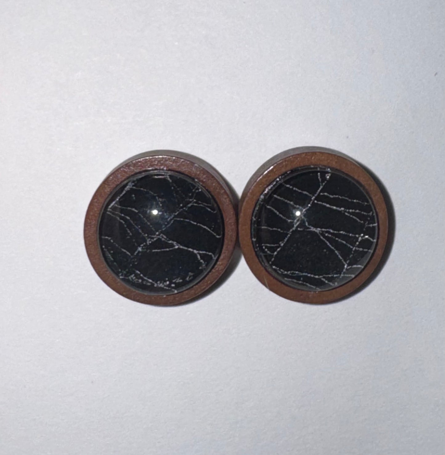 A pair of round wooden button covers with a black stone inlay featuring white veining, set against a plain off-white background.