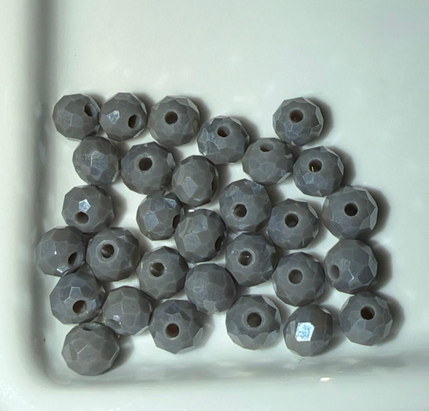 A group of faceted round gray beads with central holes, arranged in a pile inside a white ceramic dish.