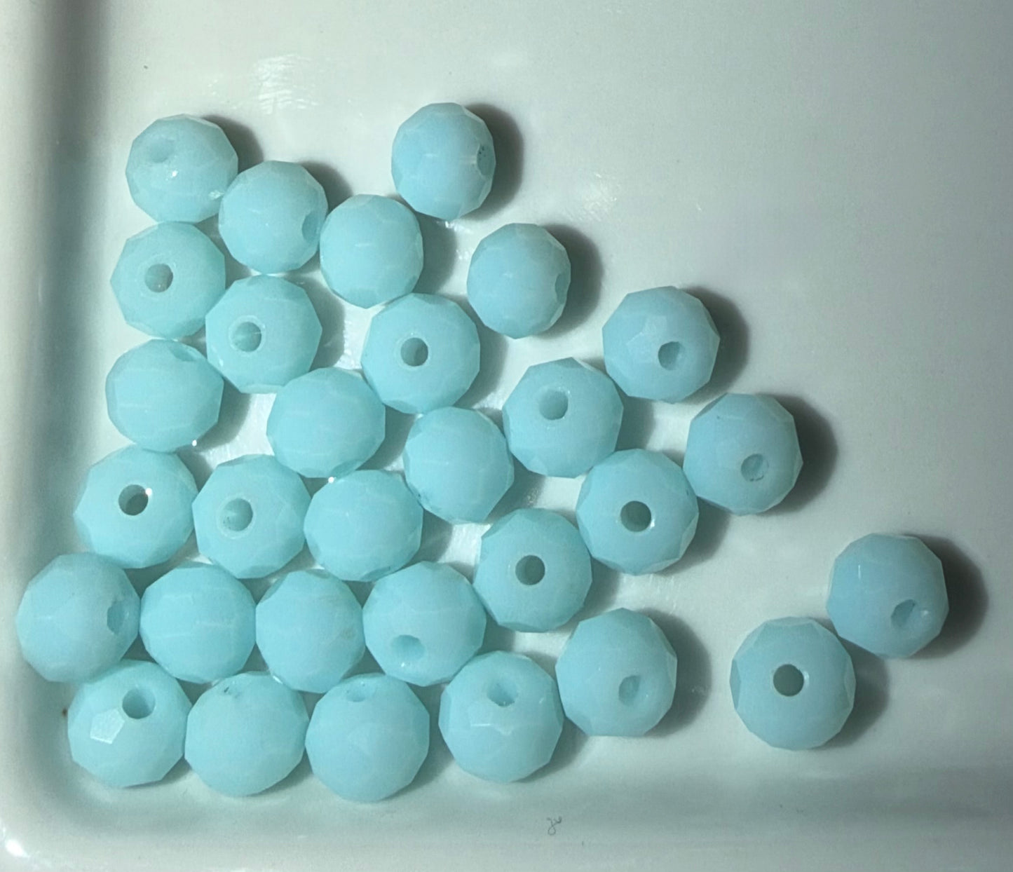 A pile of light blue faceted round beads with central holes, arranged on a white surface.