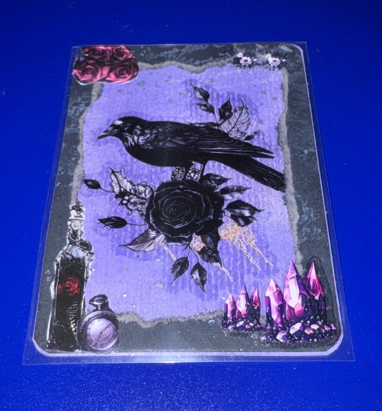 Decorative card with a crow, rose, and mystical elements on a blue background