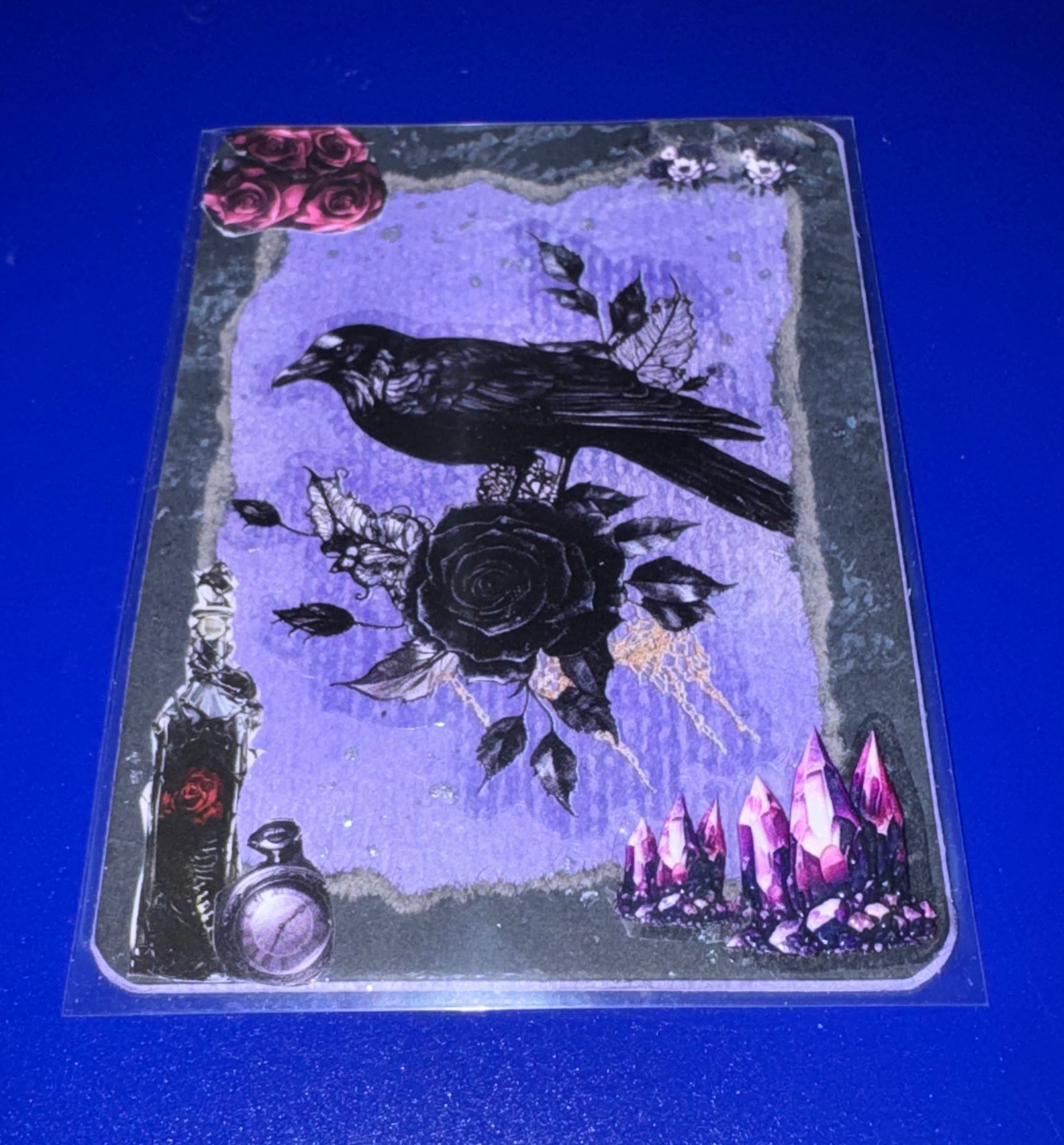 Decorative card with a crow, rose, and mystical elements on a blue background