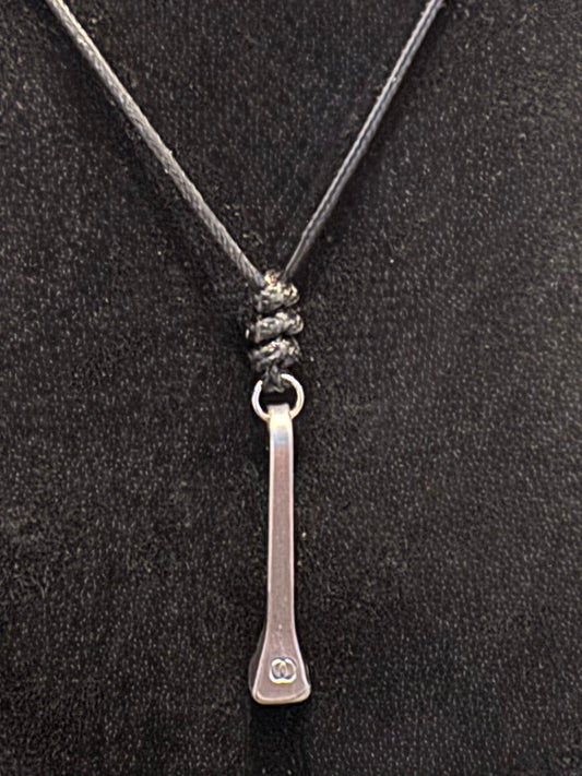 A silver-toned metal pendant necklace with a flat, elongated bar design and a small engraved double-circle logo near the bottom, suspended on a dark gray cord against a black textured background.