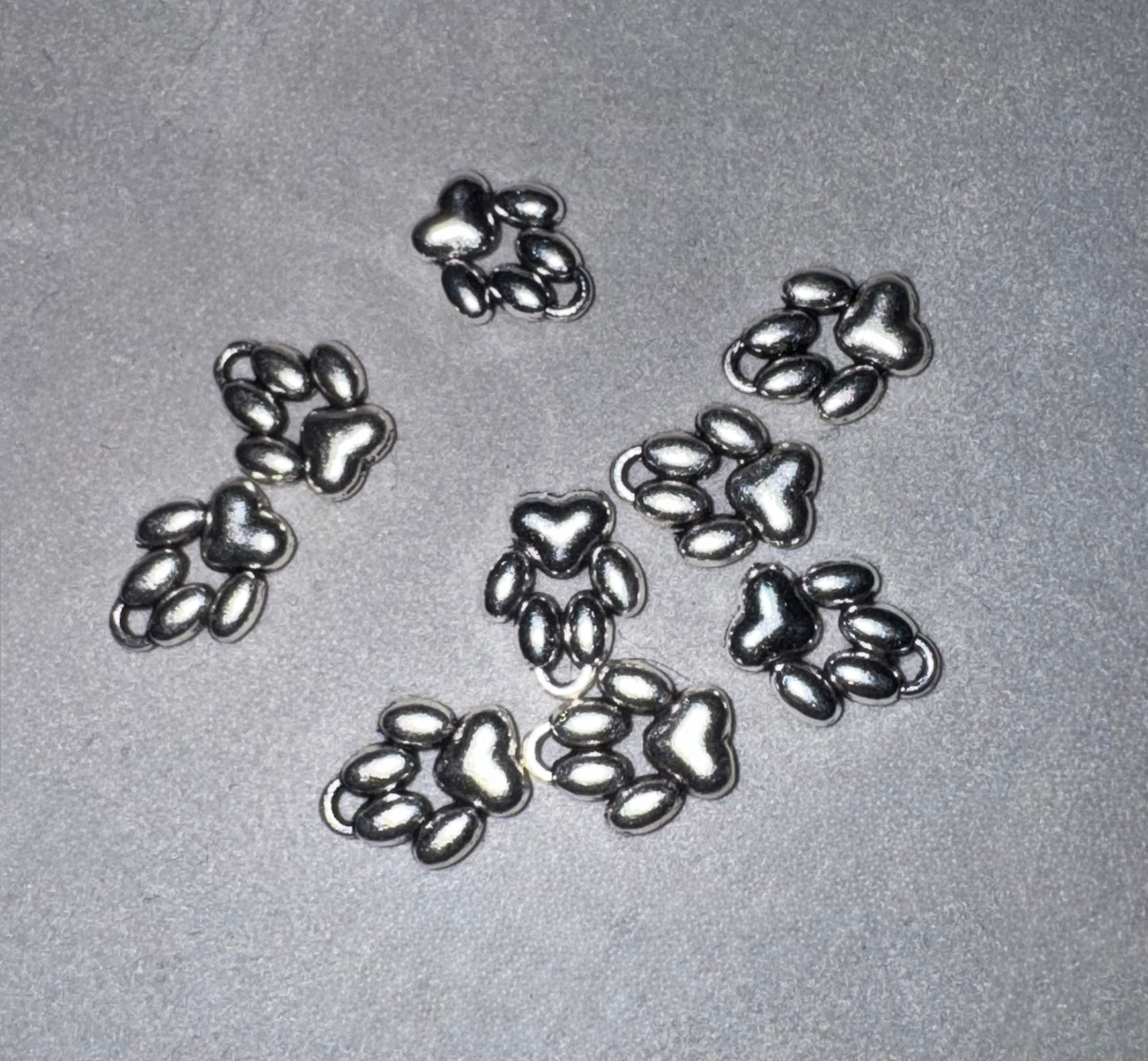 Five small metallic paw print charms arranged on a light gray textured background.