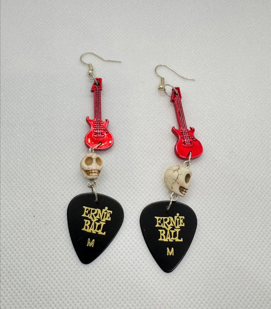 Guitar pick earrings with red guitar-shaped charms and skull beads on a gray background