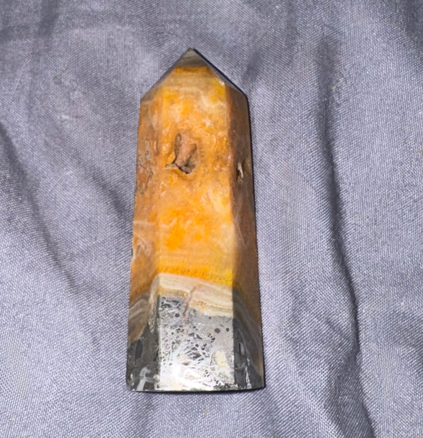 A natural quartz crystal point with a layered color profile of vibrant orange, translucent yellow, and a polished gray base, resting on a textured gray fabric background.