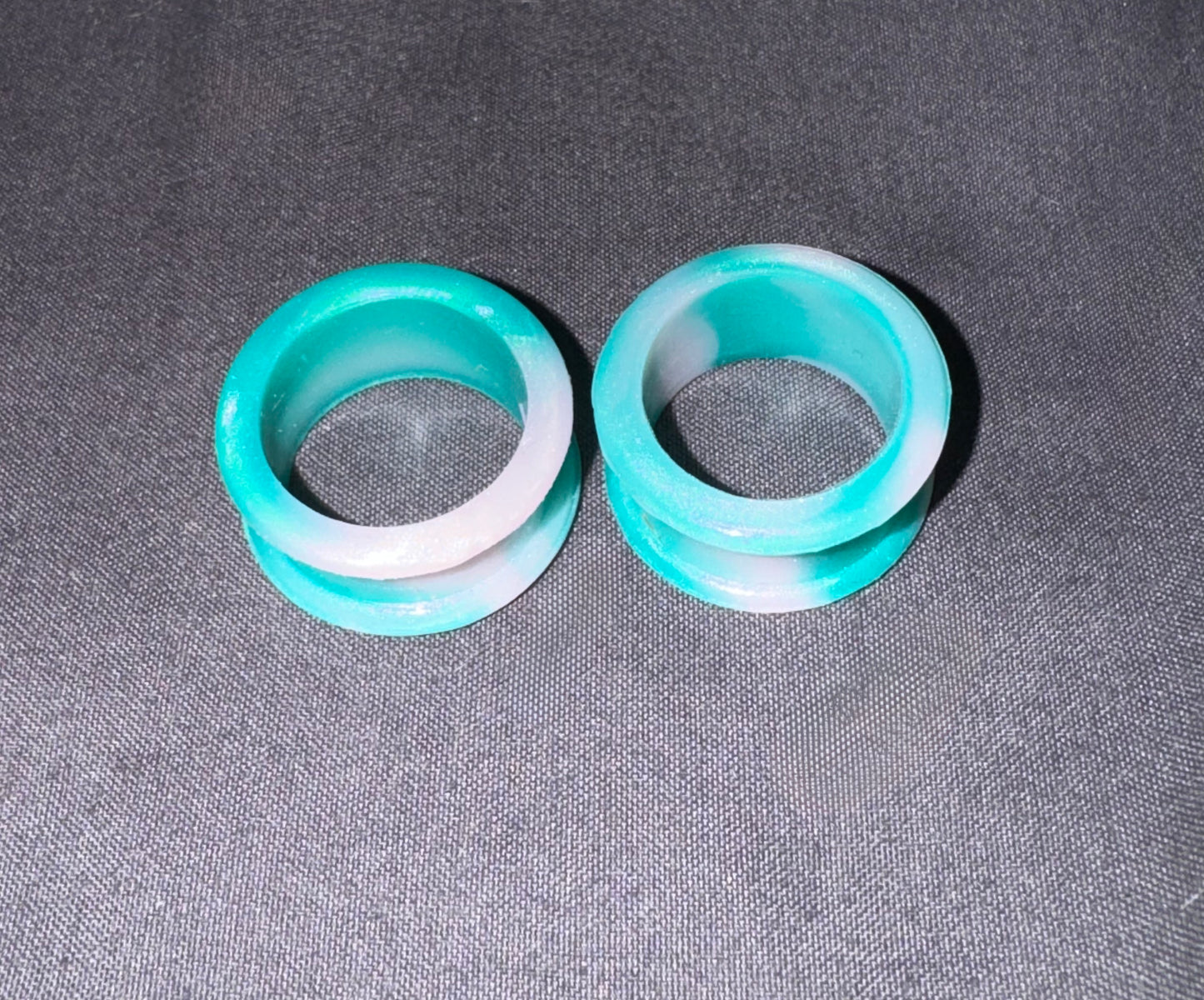 Two turquoise and white marbled plug earrings displayed on a textured gray fabric background.