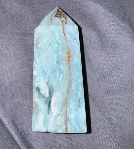 A polished  crystal point with natural brown veining, displayed on a textured gray fabric background.