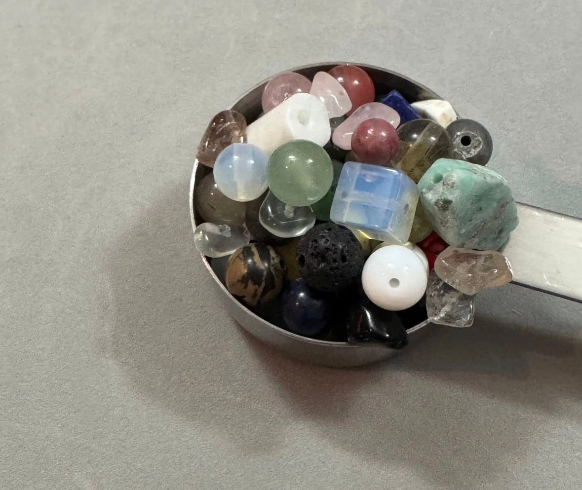Assorted gemstones in a metal container on a gray background