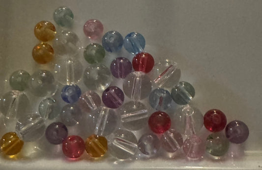 A pile of small round translucent beads in assorted colors including pink, blue, red, purple, yellow, and clear, arranged on a light neutral background.