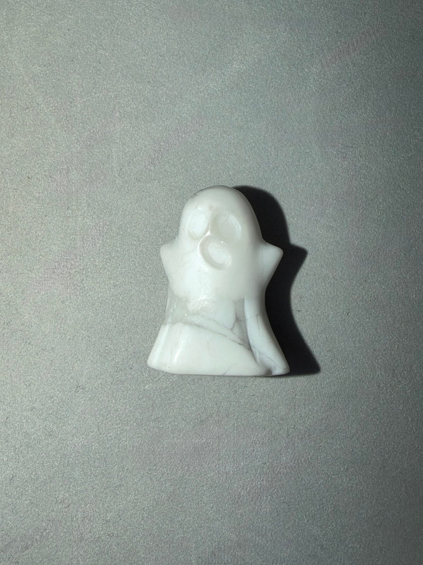 A small white carved figurine of a ghost-like character with a crescent moon face, standing on a light gray textured background.
