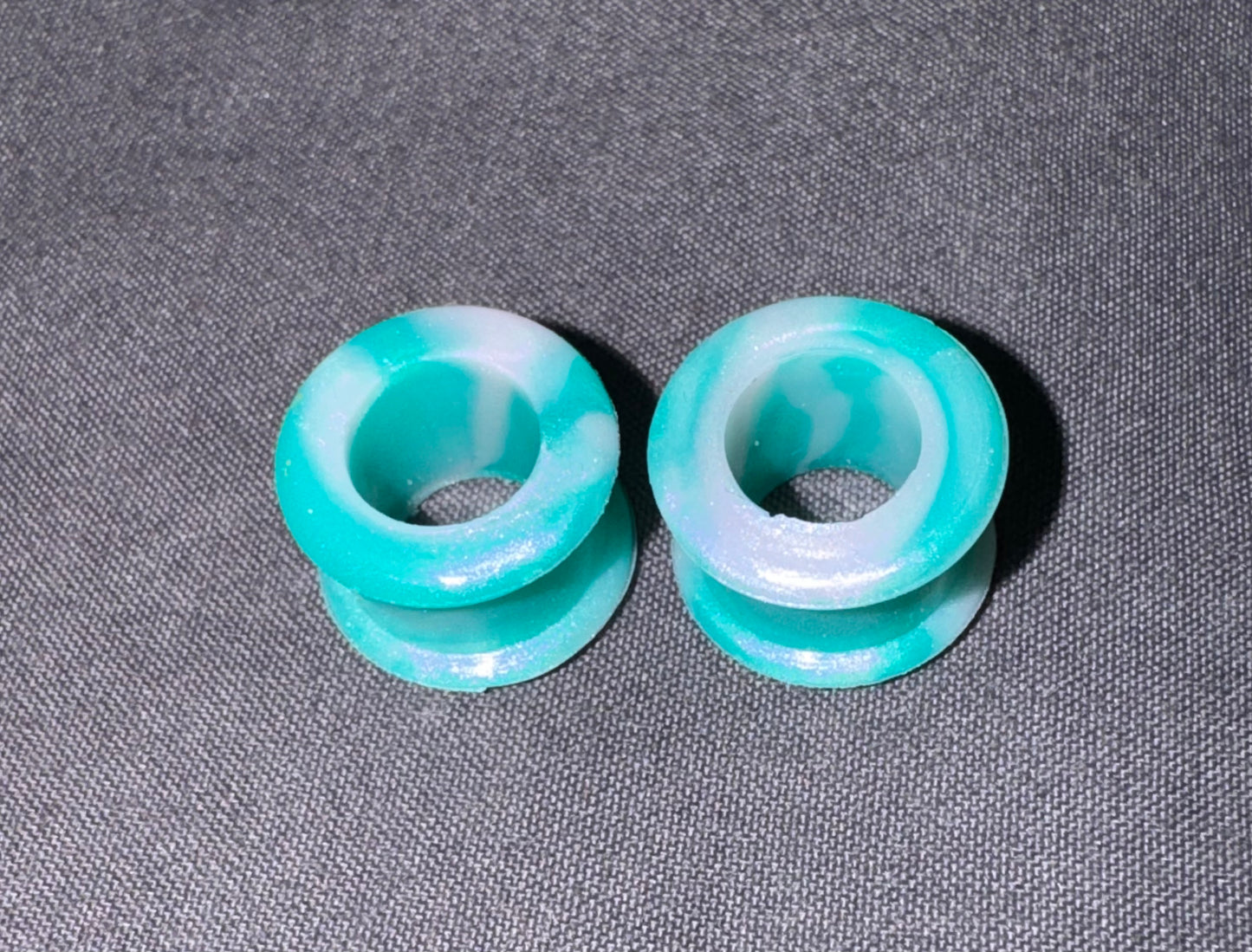 Two round turquoise and white marbled acrylic plugs on a textured gray background.