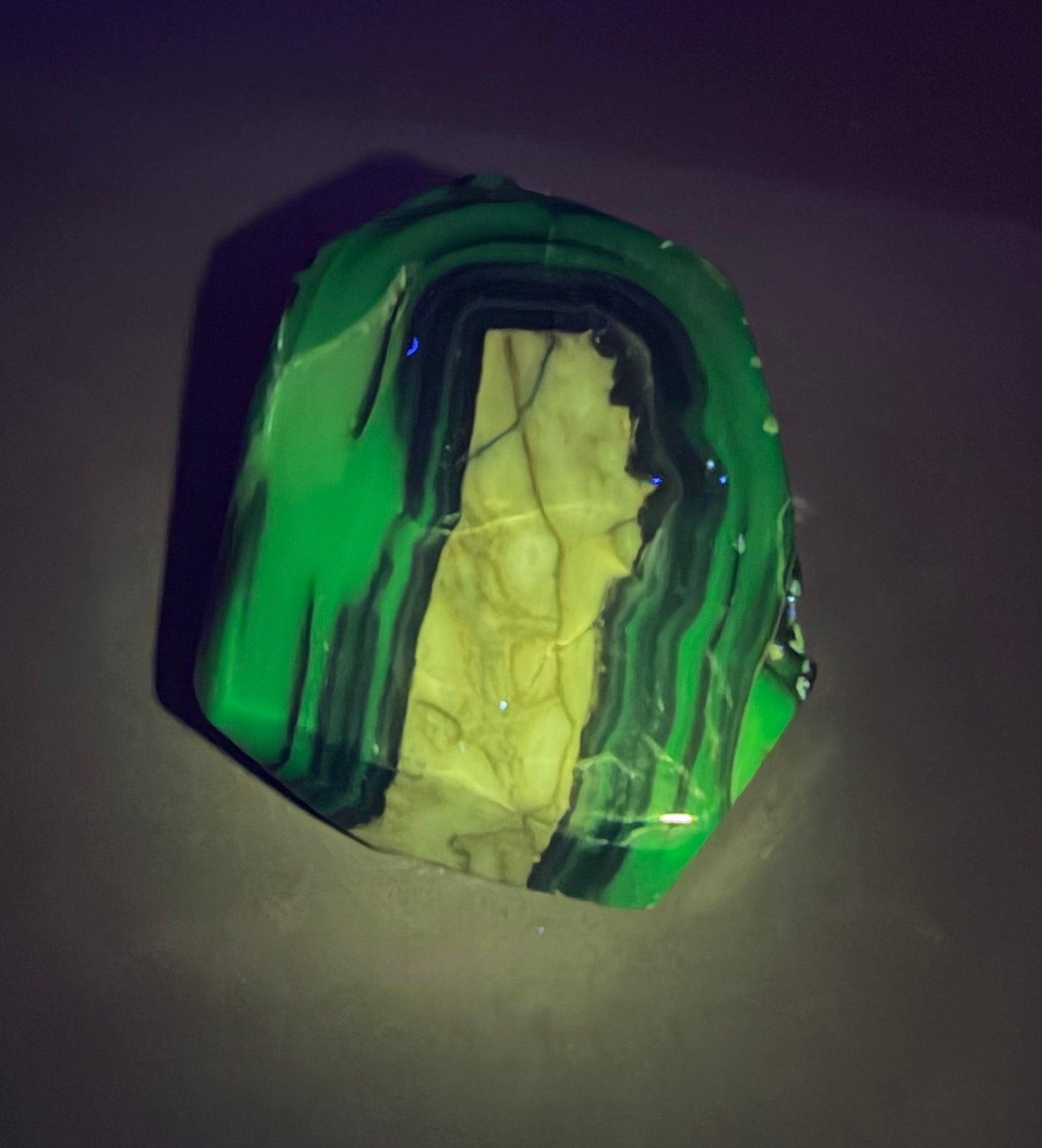 A polished volcano agate stone slab with natural banding and a yellowish interior, photographed on a dark surface under direct light.