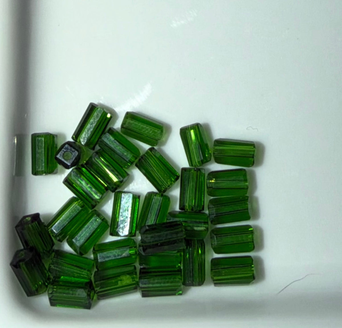 A pile of small green faceted glass beads scattered on a white surface.