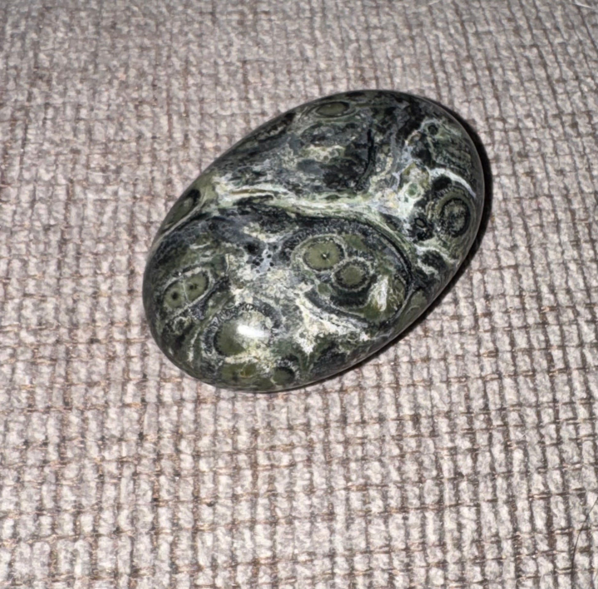 Kambaba Jasper stone with swirling patterns on a textured fabric background