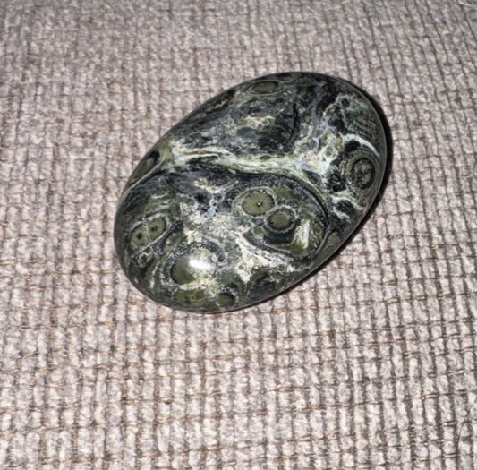 Kambaba Jasper stone with swirling patterns on a textured fabric background