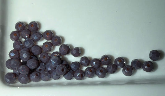 Faceted round beads in a dusty purple color with a small orange-brown center, arranged on a white surface.