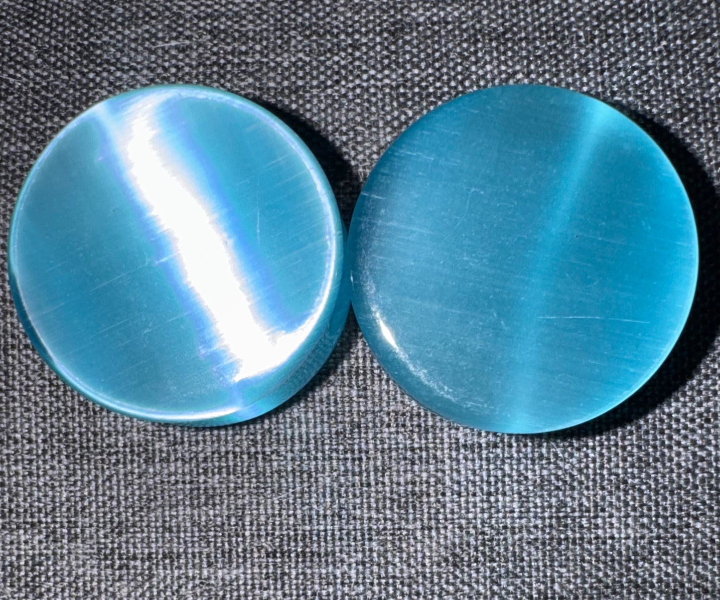 Two blue cat's eye ear gauges on a textured gray surface