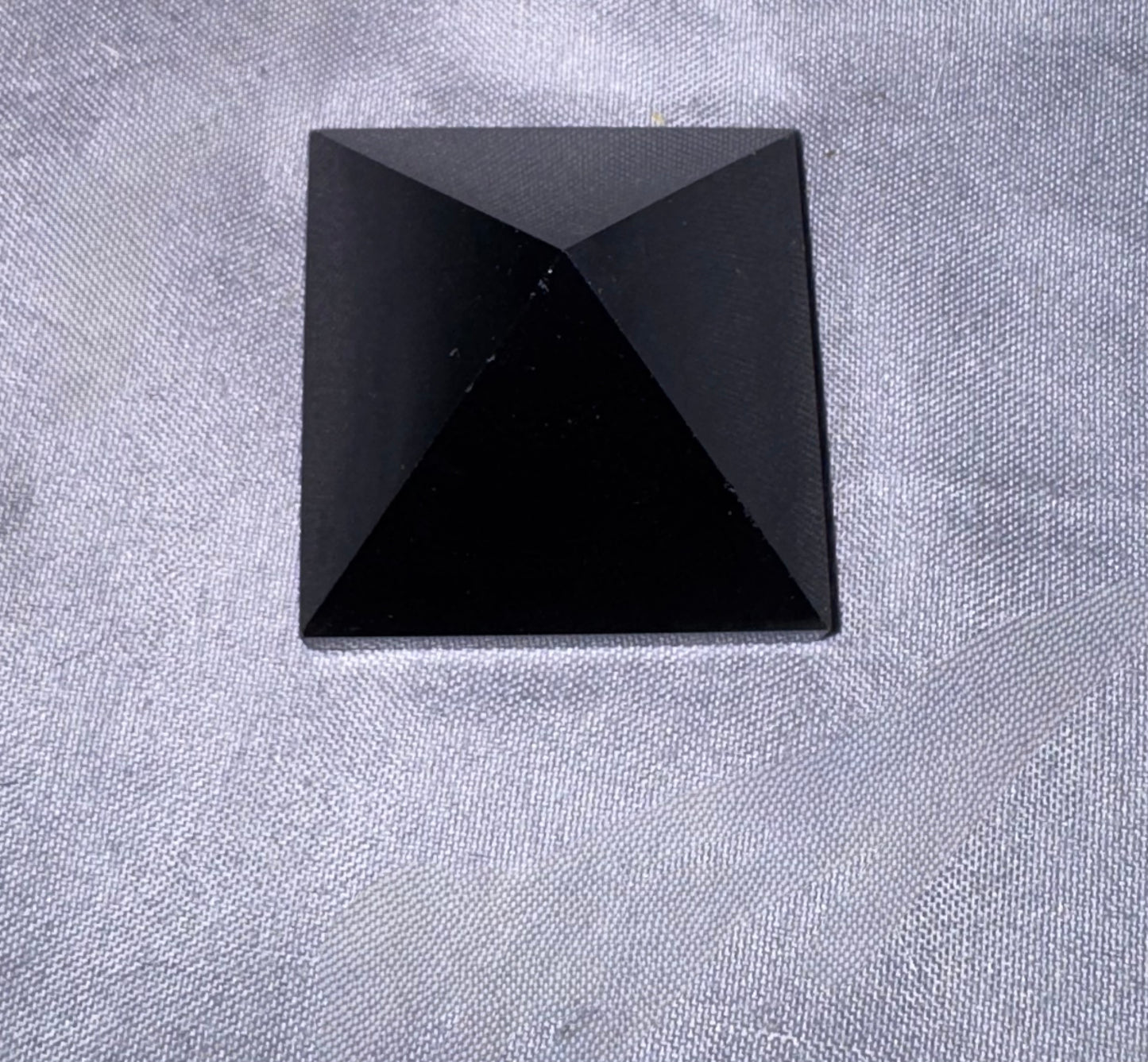 A faceted black pyramid stone cabochon resting on a textured light gray fabric background.