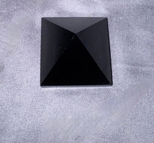 A faceted black pyramid stone cabochon resting on a textured light gray fabric background.