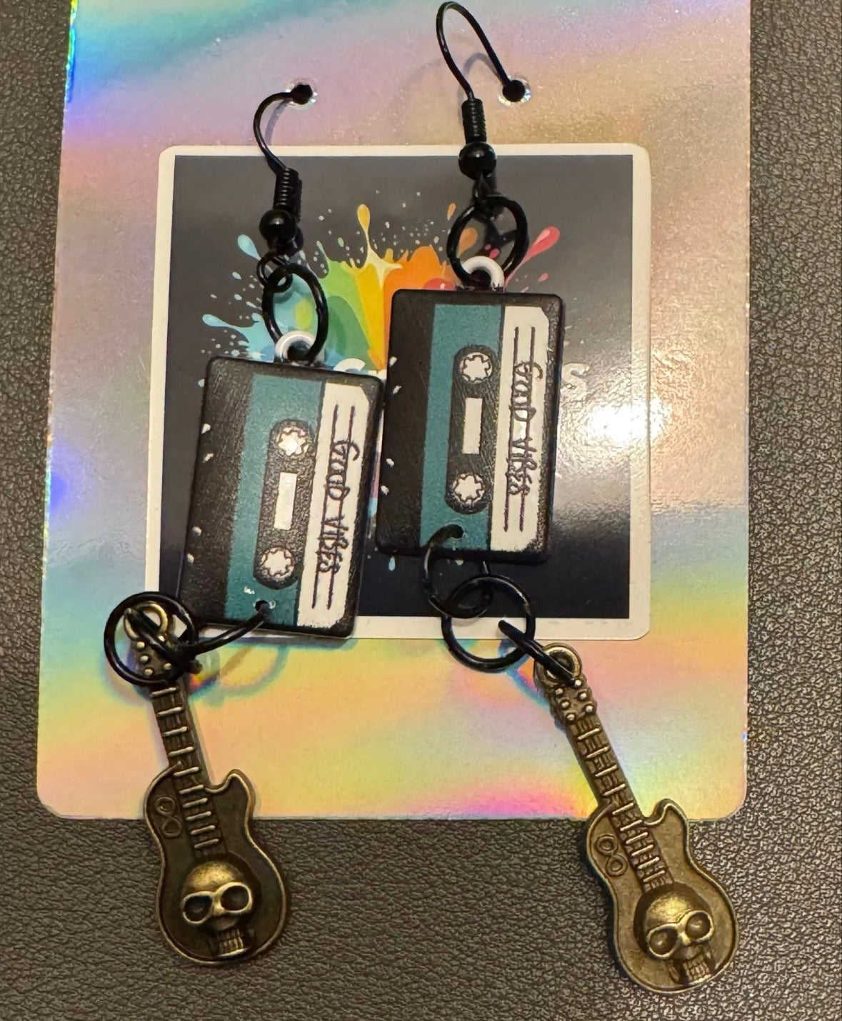 Cassette tape and guitar-shaped earrings on a colorful card with a rainbow gradient.
