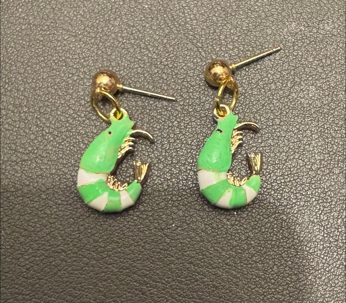 Green and white shrimp-shaped earrings on a gray textured background