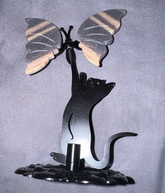 A decorative metal sculpture of a black cat reaching up toward a butterfly with patterned wings, mounted on a dark base against a textured gray background.