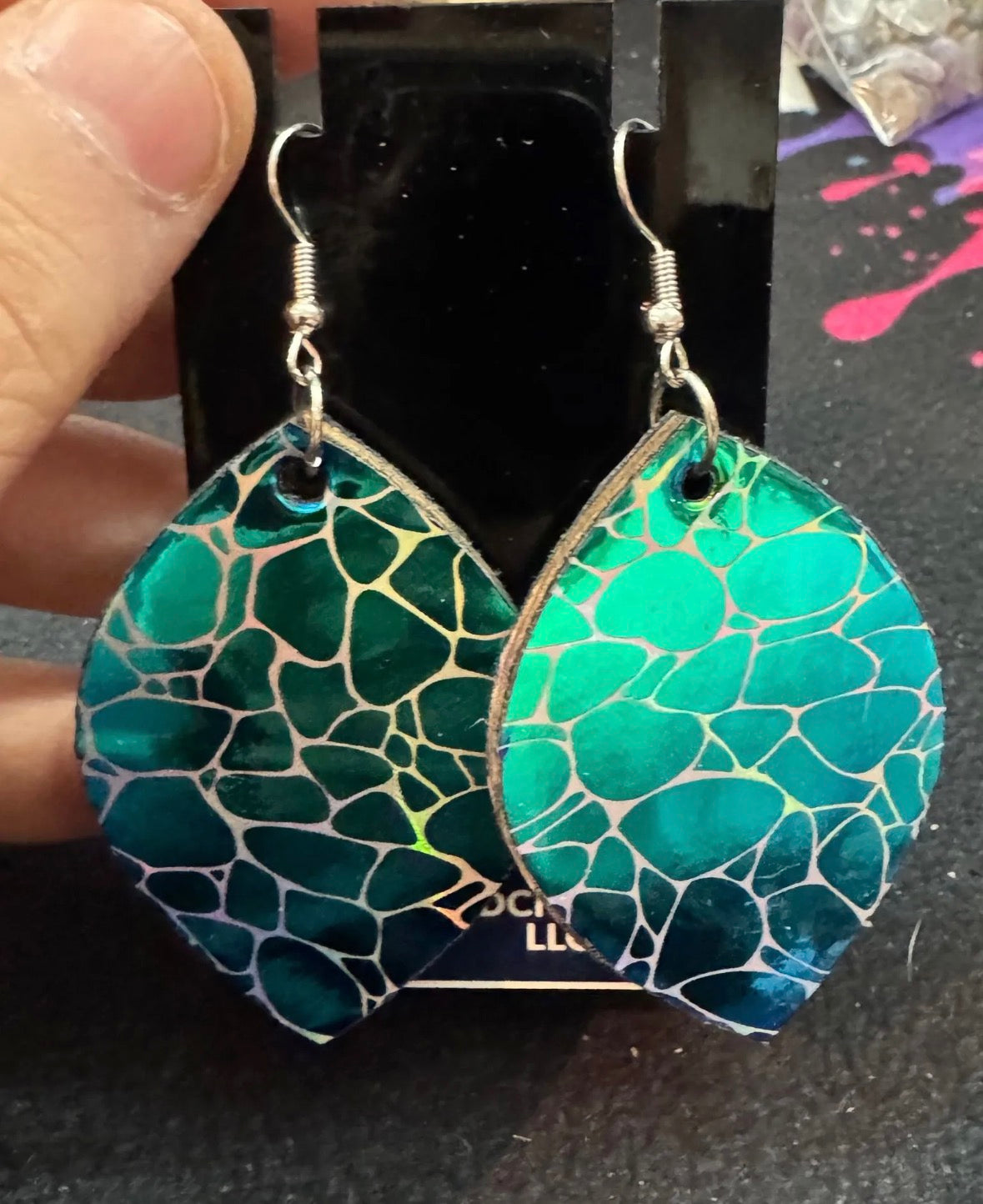 Green mosaic patterned earrings held against a dark background
