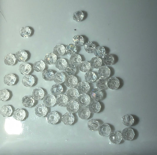 A pile of small, round, faceted clear glass beads scattered on a light gray surface.