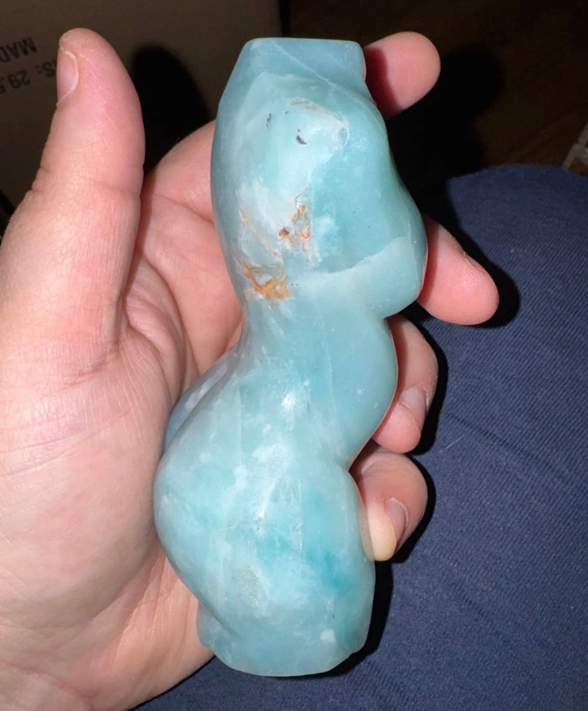 Hand holding a light blue stone object against a dark background