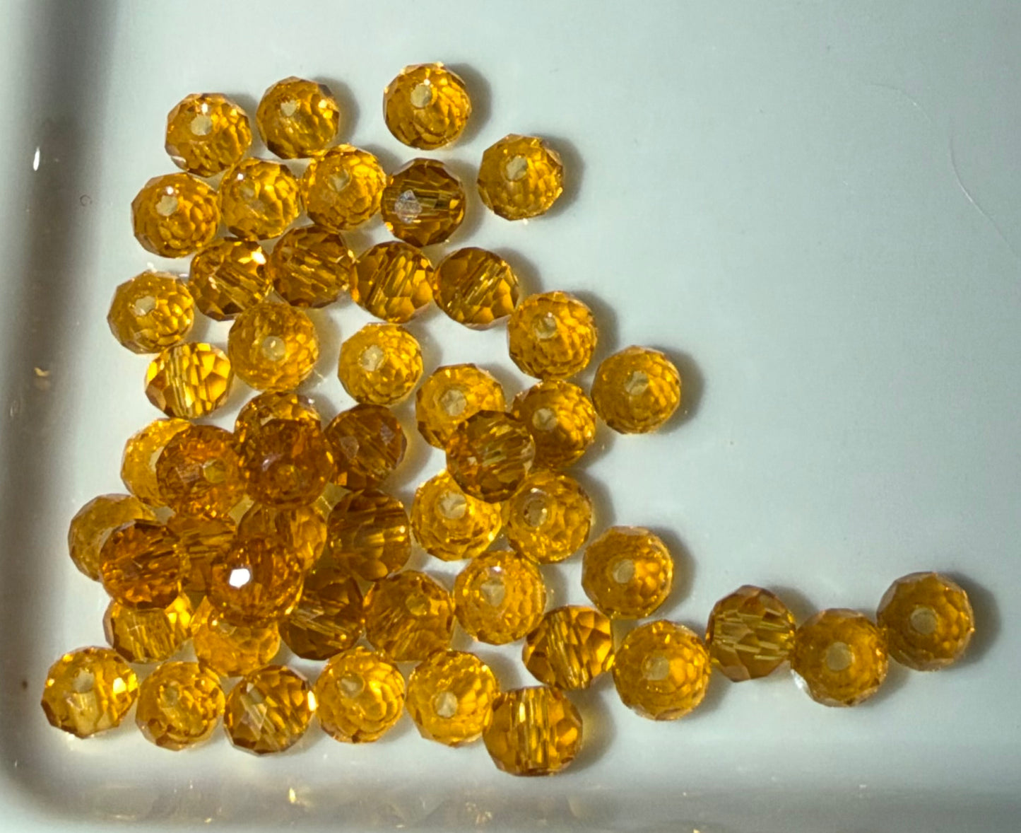 A pile of faceted amber-yellow glass beads scattered on a plain white surface.