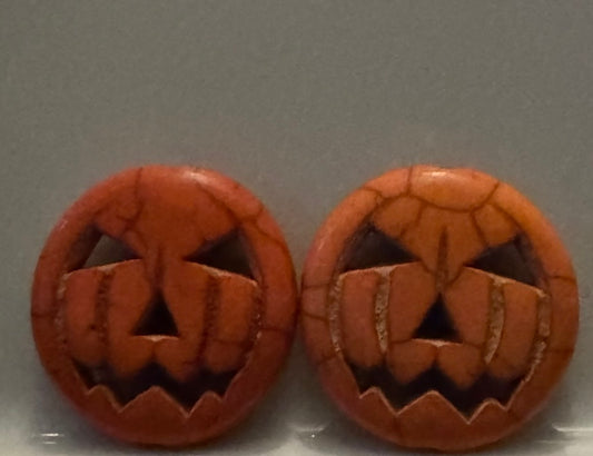 A pair of round orange jack-o'-lantern face beads with a cracked clay-like texture, displayed side-by-side on a neutral gray background.