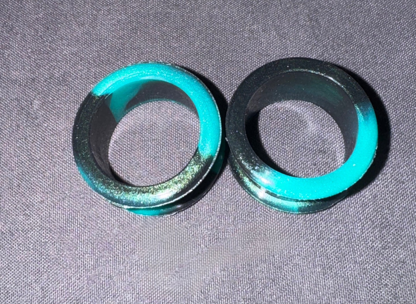 Two circular black rings with a bright turquoise green inner coating, displayed on a textured gray fabric background.