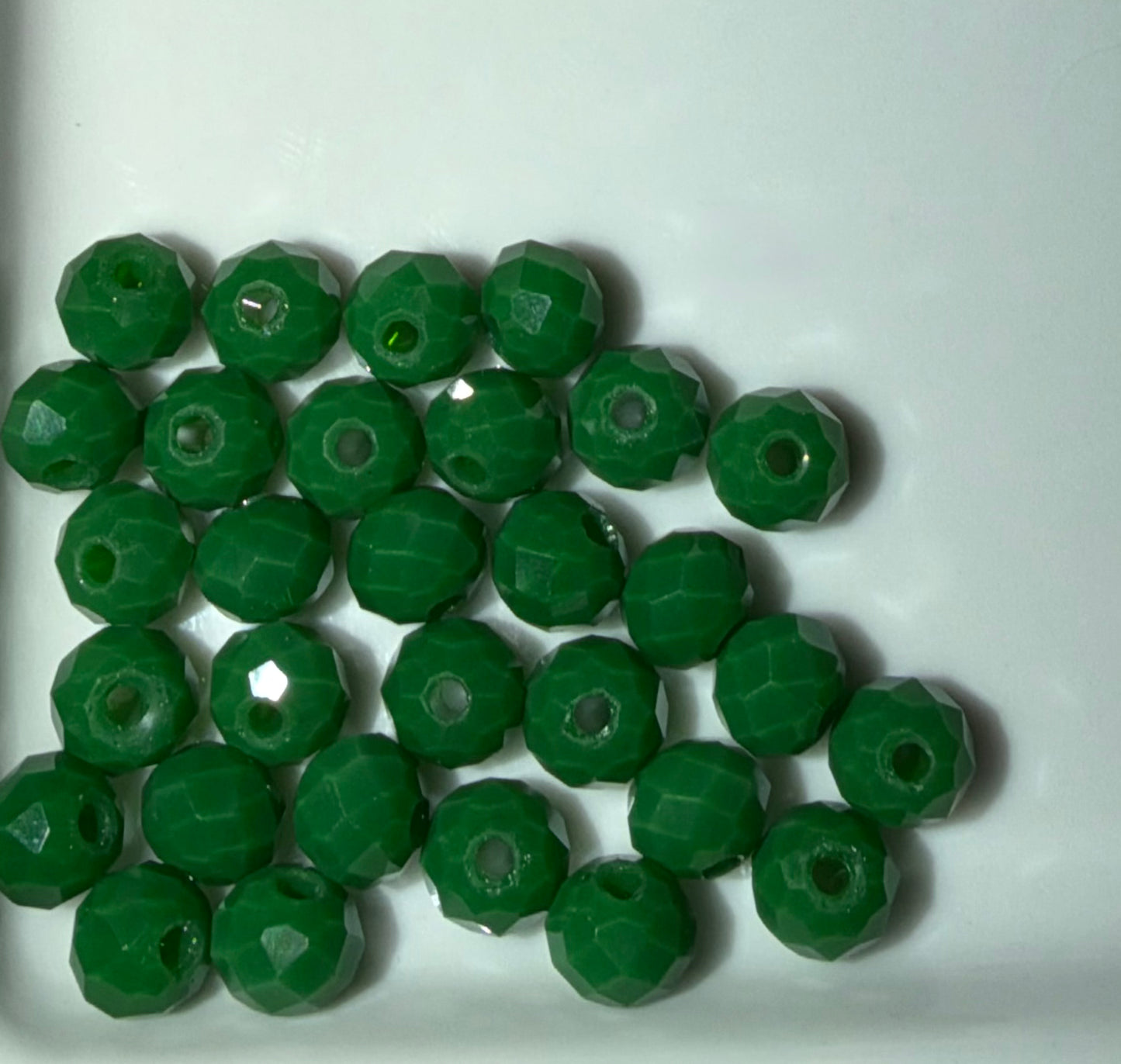 A pile of faceted green glass beads with central holes, arranged on a plain white surface.
