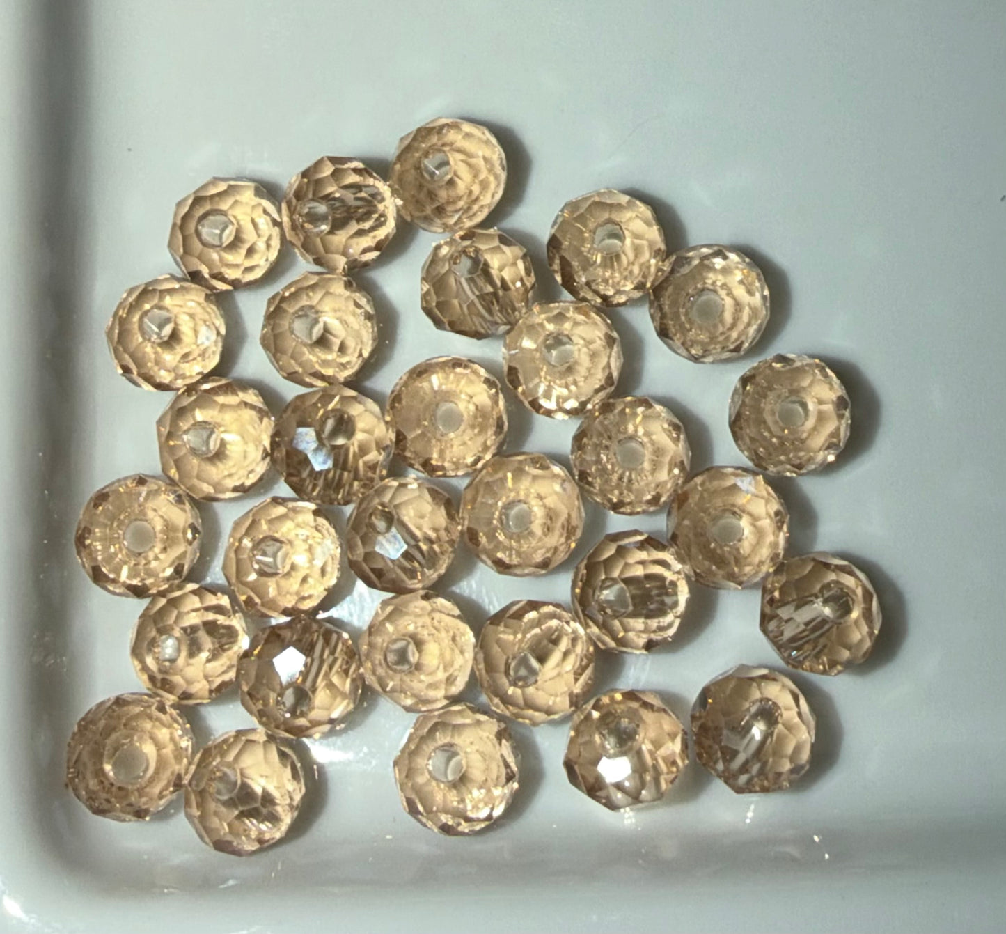 A pile of faceted round glass beads in a light gold or champagne color, arranged on a white surface.