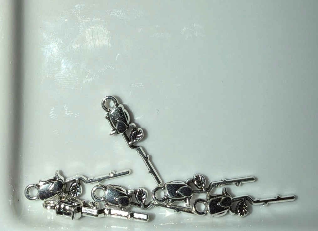 Several silver rose charms scattered on a white surface.