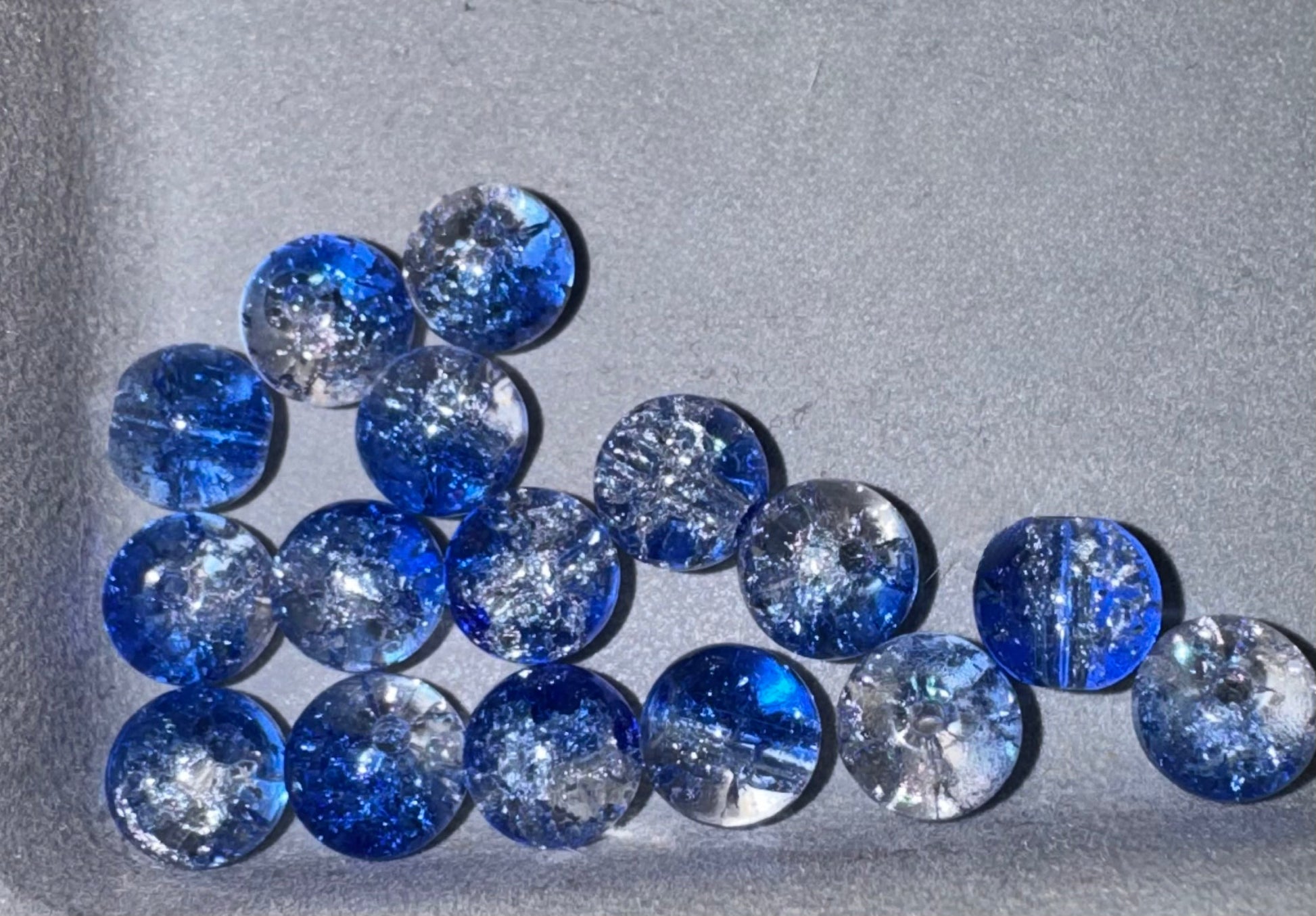A group of round blue and clear glass beads with crackle , arranged on a textured gray background.