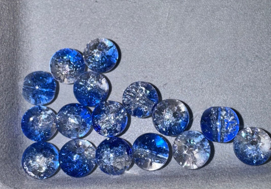 A group of round blue and clear glass beads with crackle , arranged on a textured gray background.