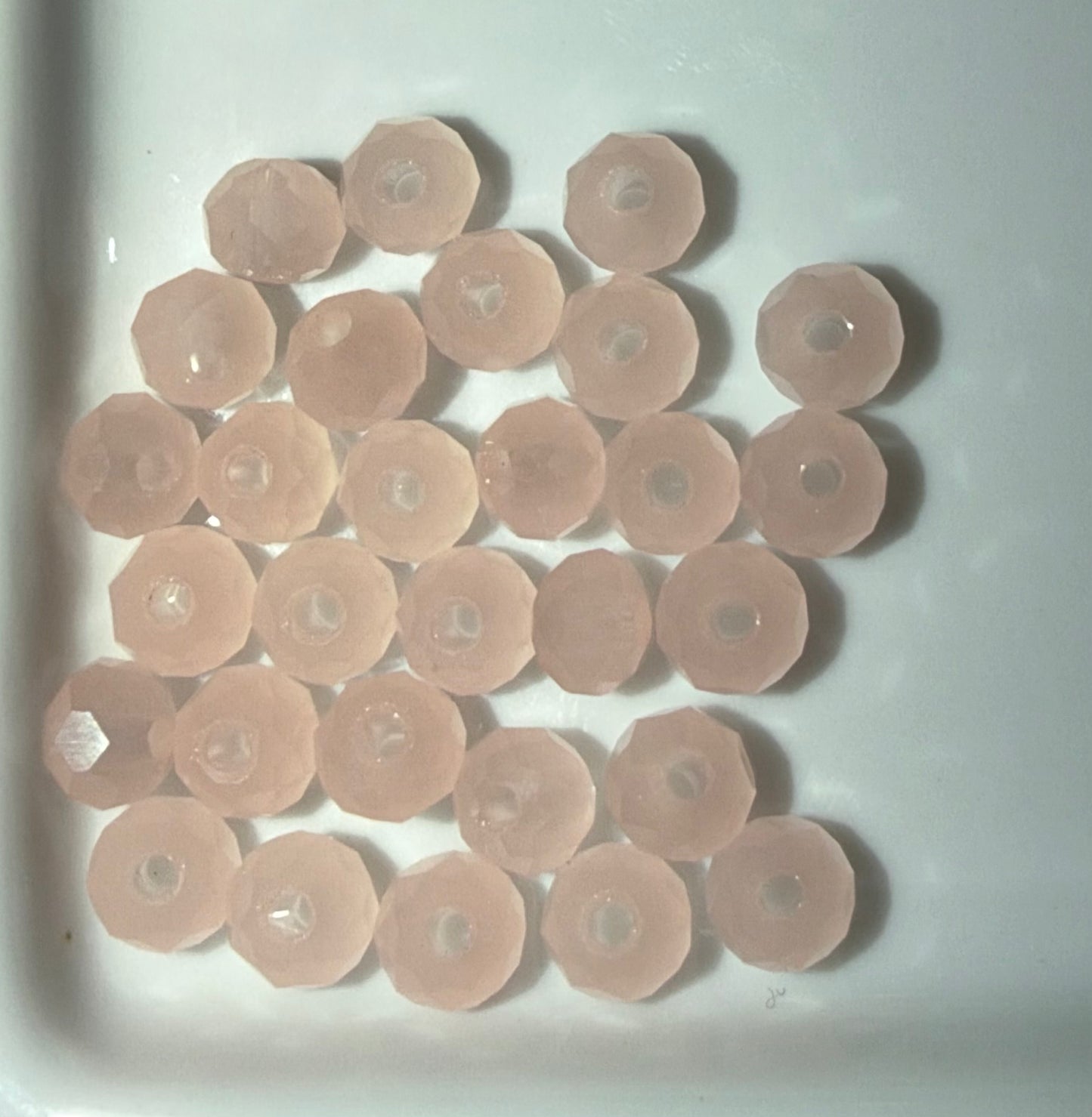 A group of small, pale pink faceted circular beads with central holes, arranged on a white surface.