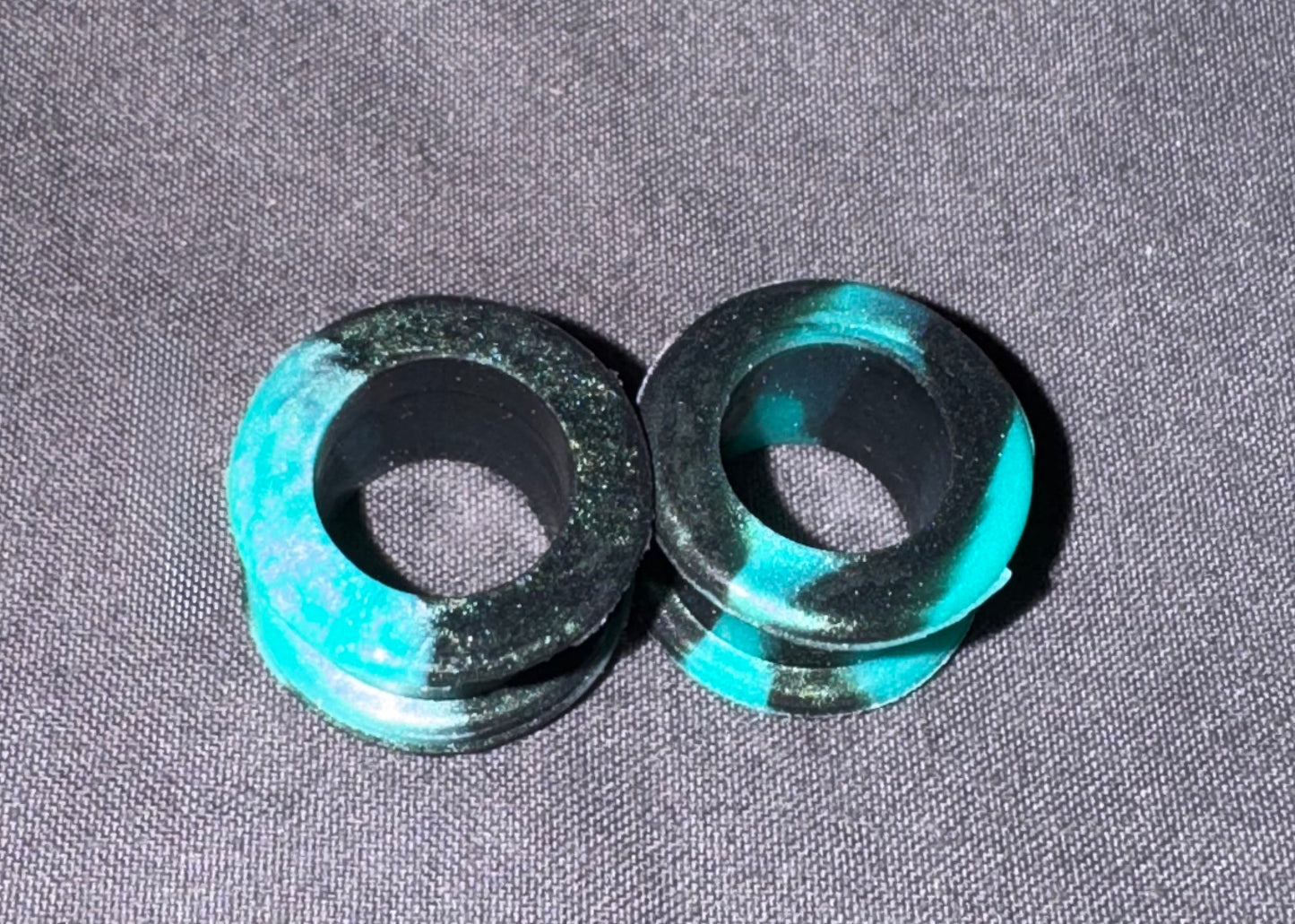 Two circular black and turquoise marbled plug-on earrings or rings displayed on a textured gray fabric background.