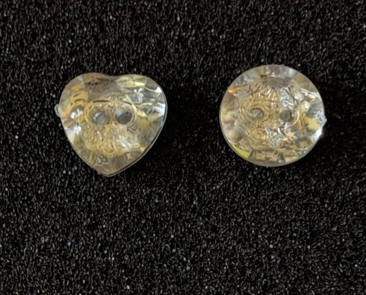 Two clear glass beads, one heart-shaped and one round, displayed on a black textured background.