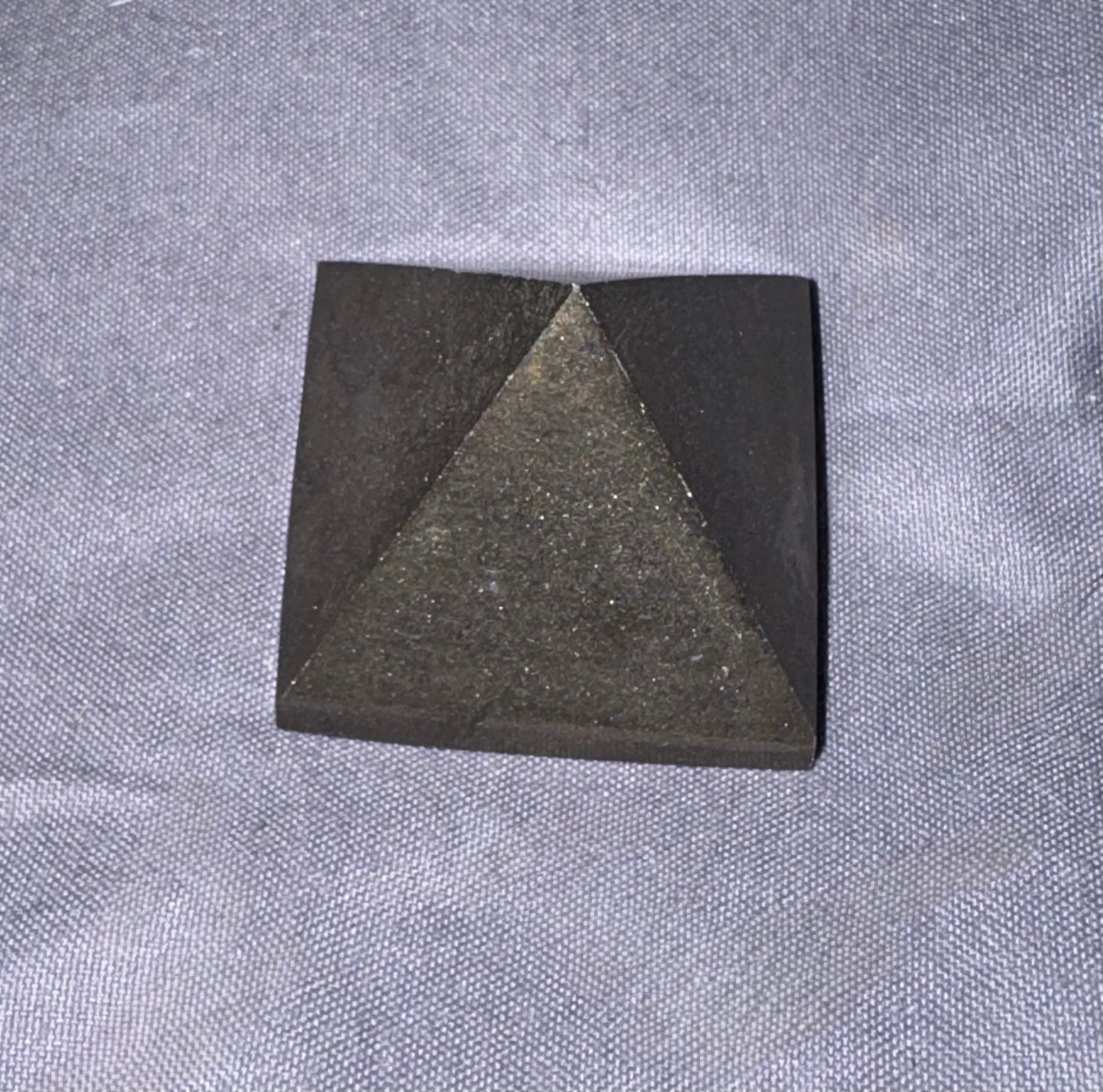 A small black pyramid-shaped stone or ceramic object placed on a textured gray fabric background.